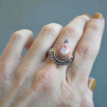 Hand wearing a ring with a pink stone against a gray background