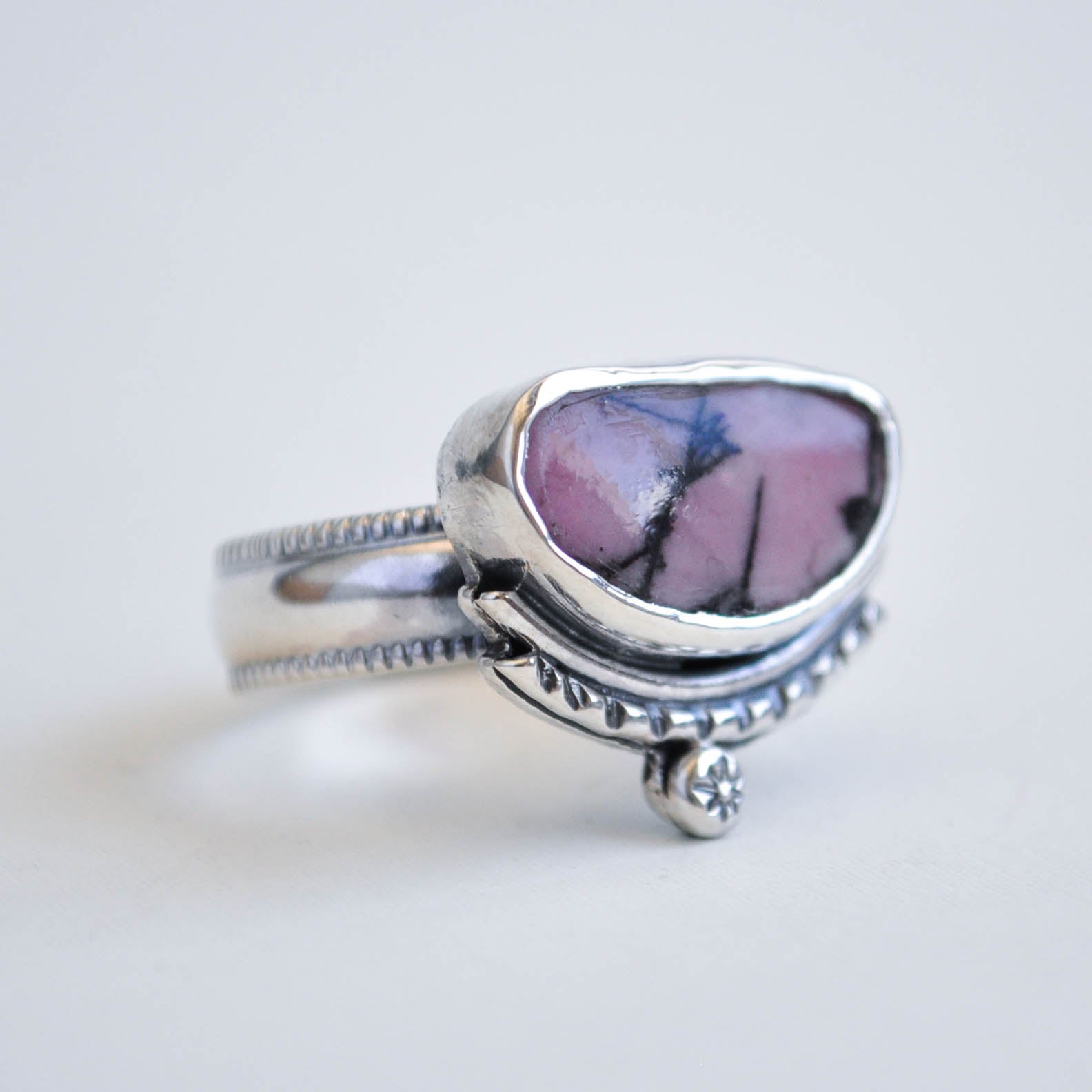 Silver ring with a pink and purple stone on a light gray background