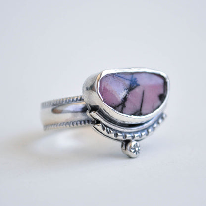 Silver ring with a pink and purple stone on a light gray background
