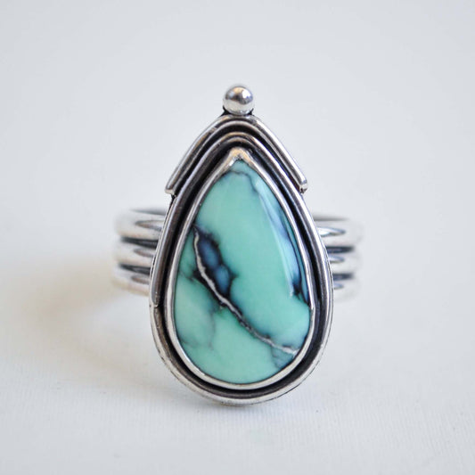 Turquoise teardrop ring with silver band on a light gray background