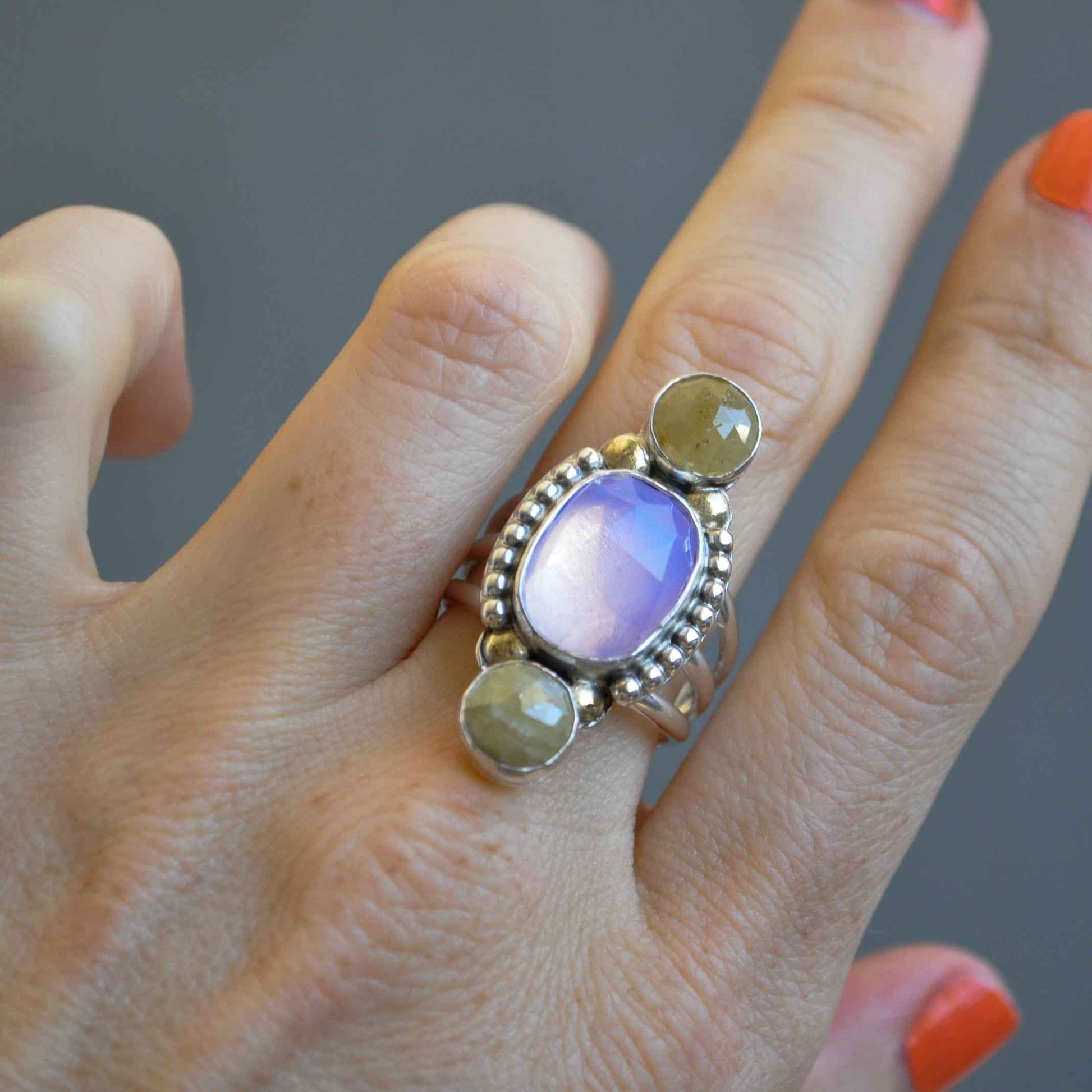 Hand wearing a ring with multicolored stones on a neutral background