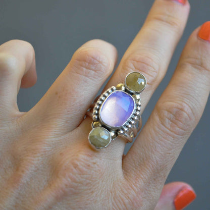 Hand wearing a ring with multicolored stones on a neutral background