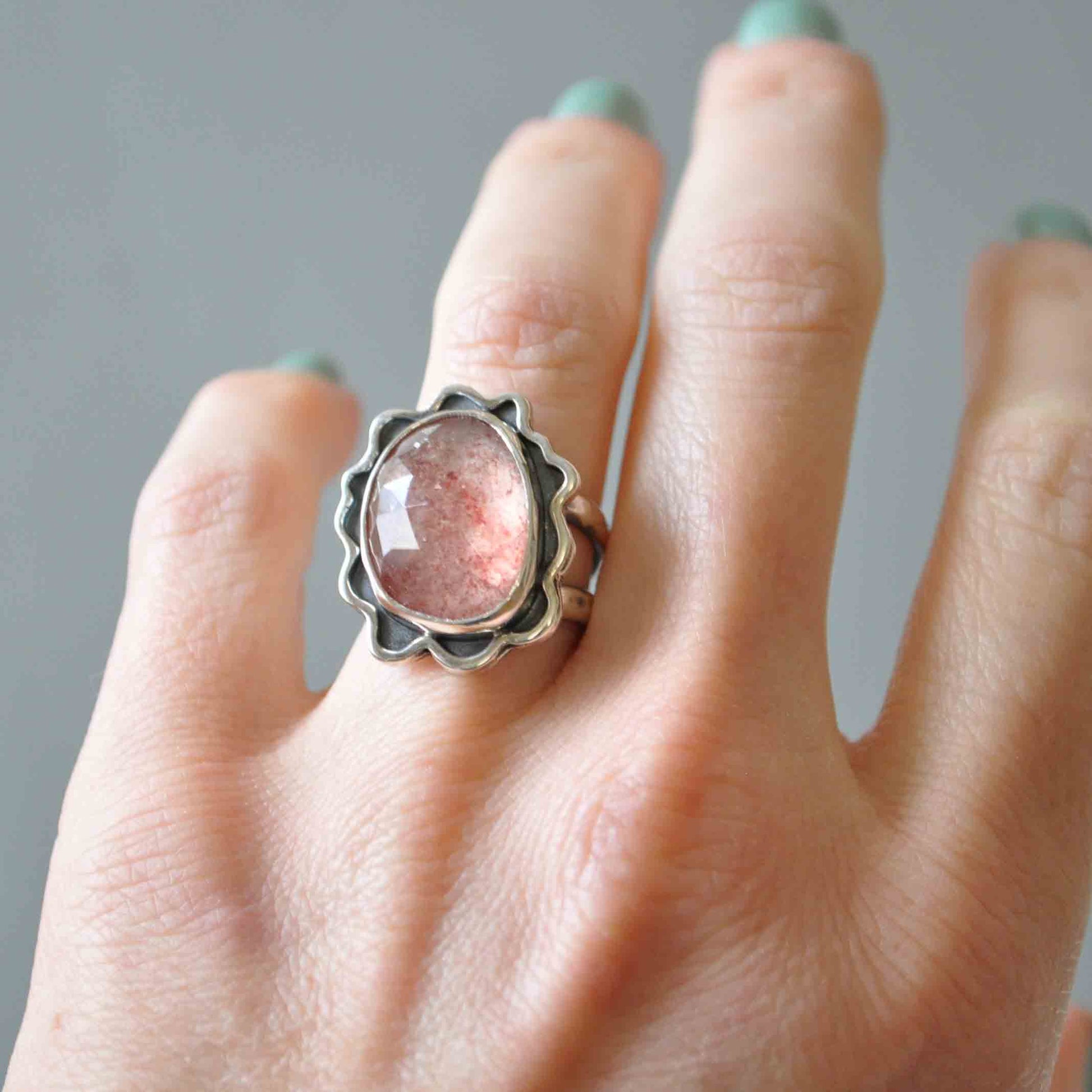 Hand wearing a ring with a pink stone against a neutral background