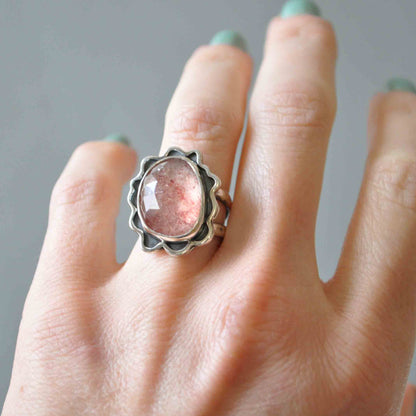 Hand wearing a ring with a pink stone against a neutral background