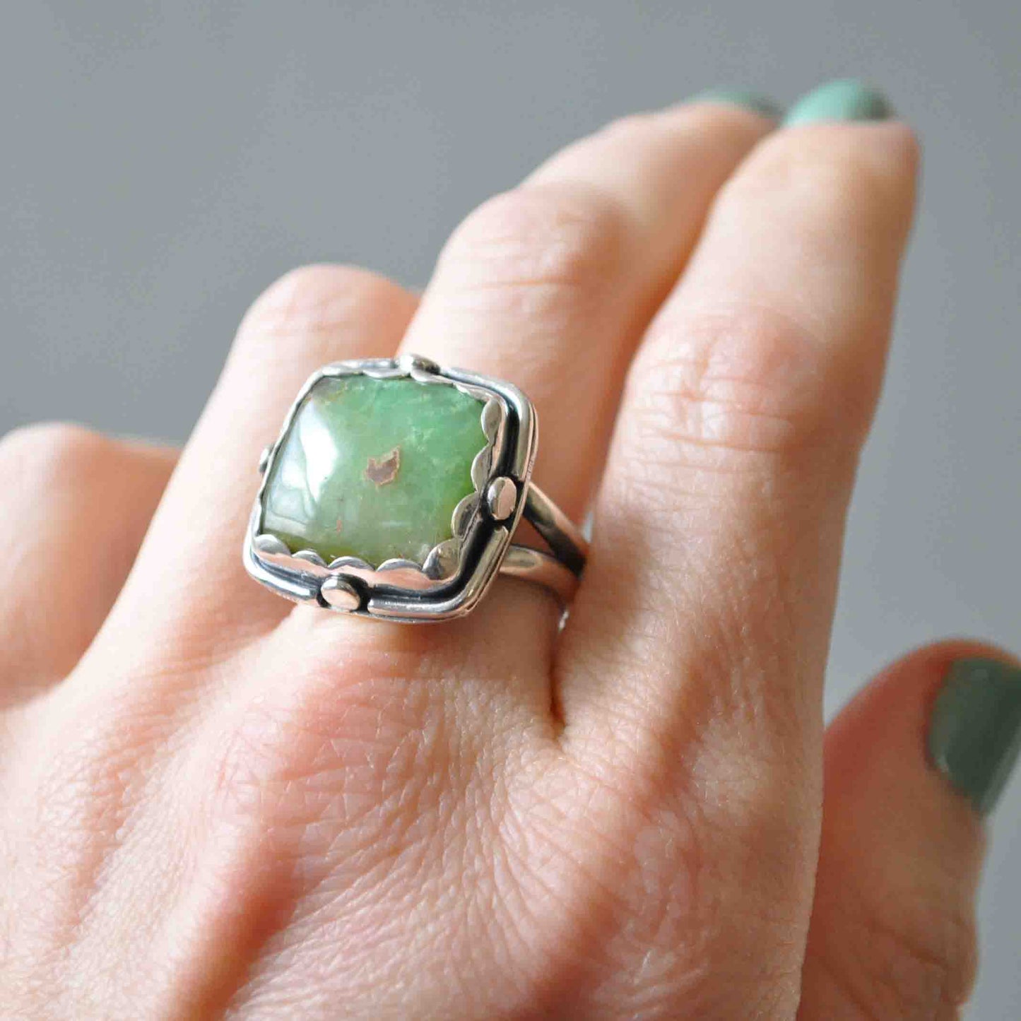 Silver ring with a green stone on a person's finger against a neutral background