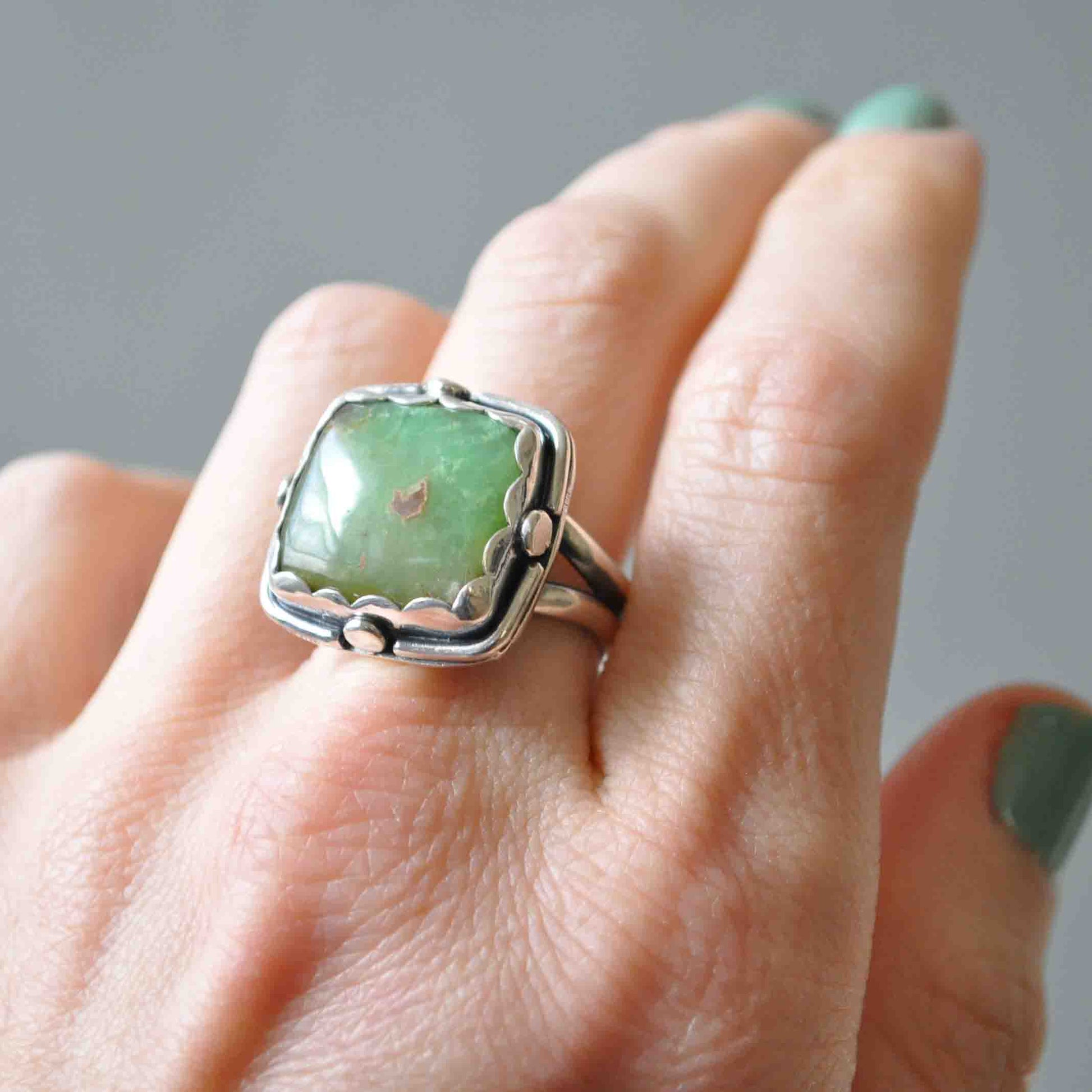 Silver ring with a green stone on a person's finger against a neutral background