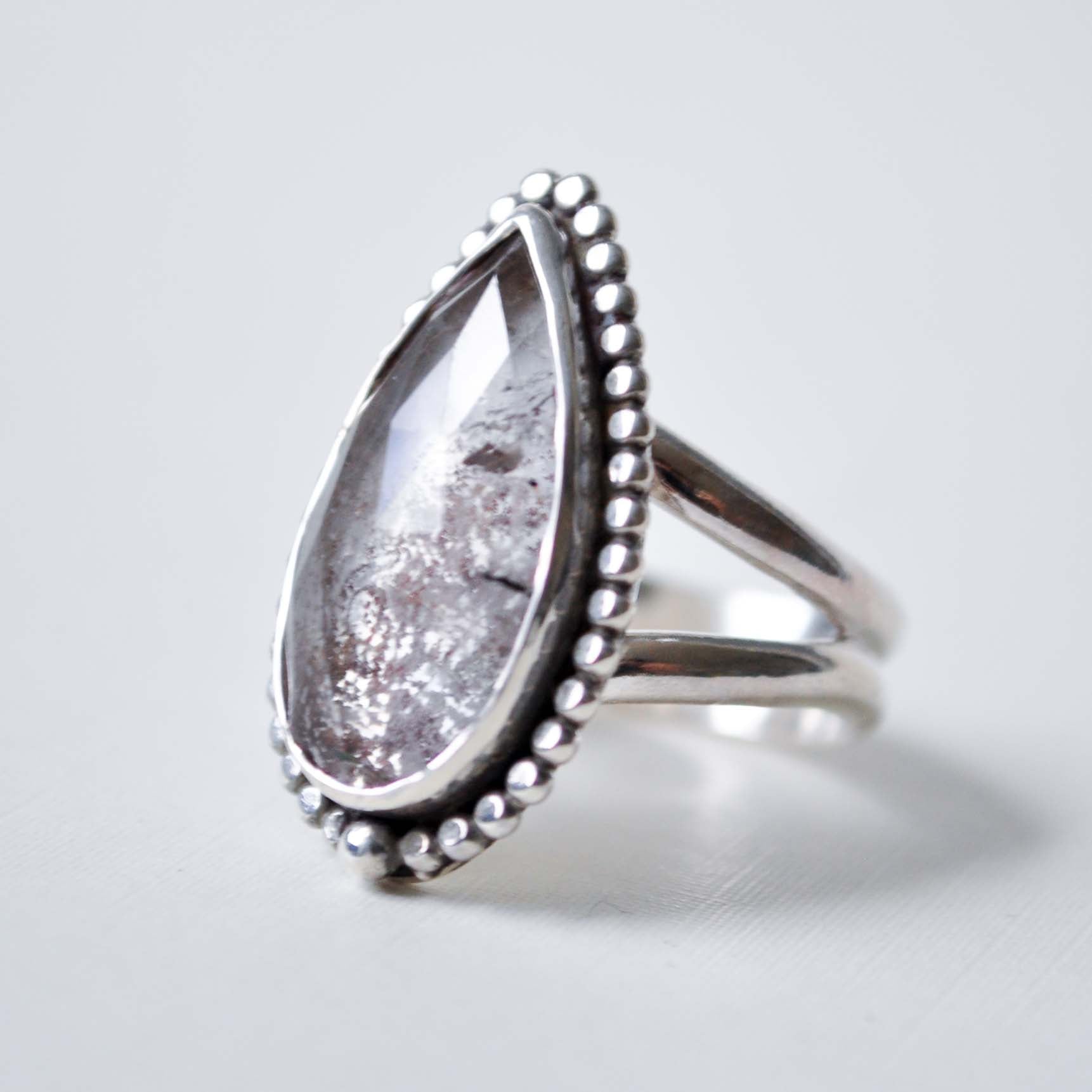 Silver ring with a teardrop-shaped gemstone on a light gray background