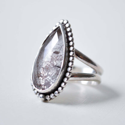 Silver ring with a teardrop-shaped gemstone on a light gray background