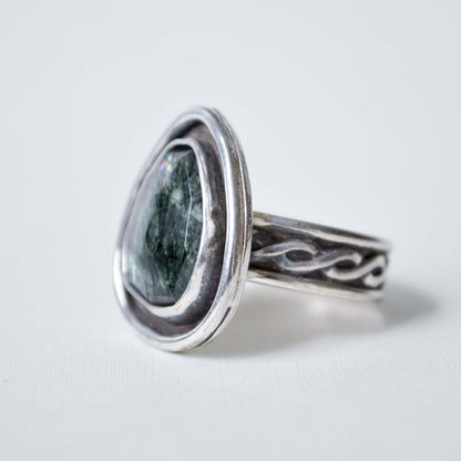 Silver ring with a green stone on a light gray background