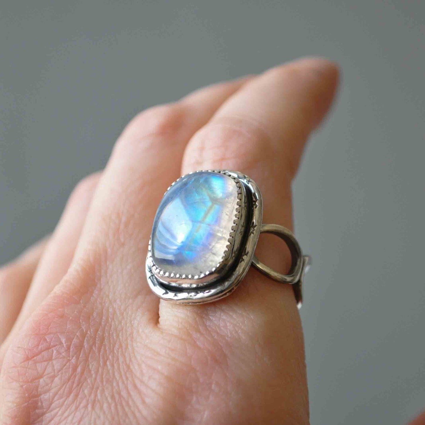 Silver ring with a rainbow moonstone on a hand against a gray background