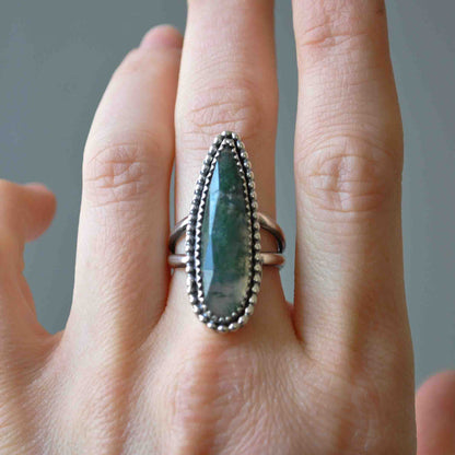 Silver ring with a green stone on a finger against a neutral background