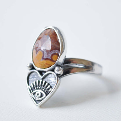 Silver ring with heart design and amber stone on a light gray background