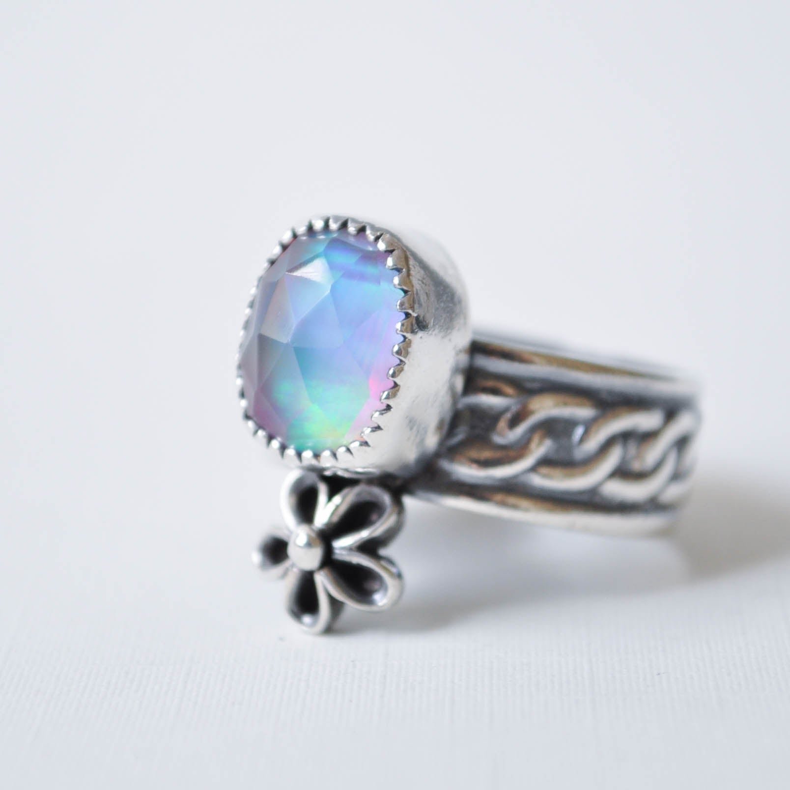 Silver ring with a colorful gemstone and floral charm on a white background