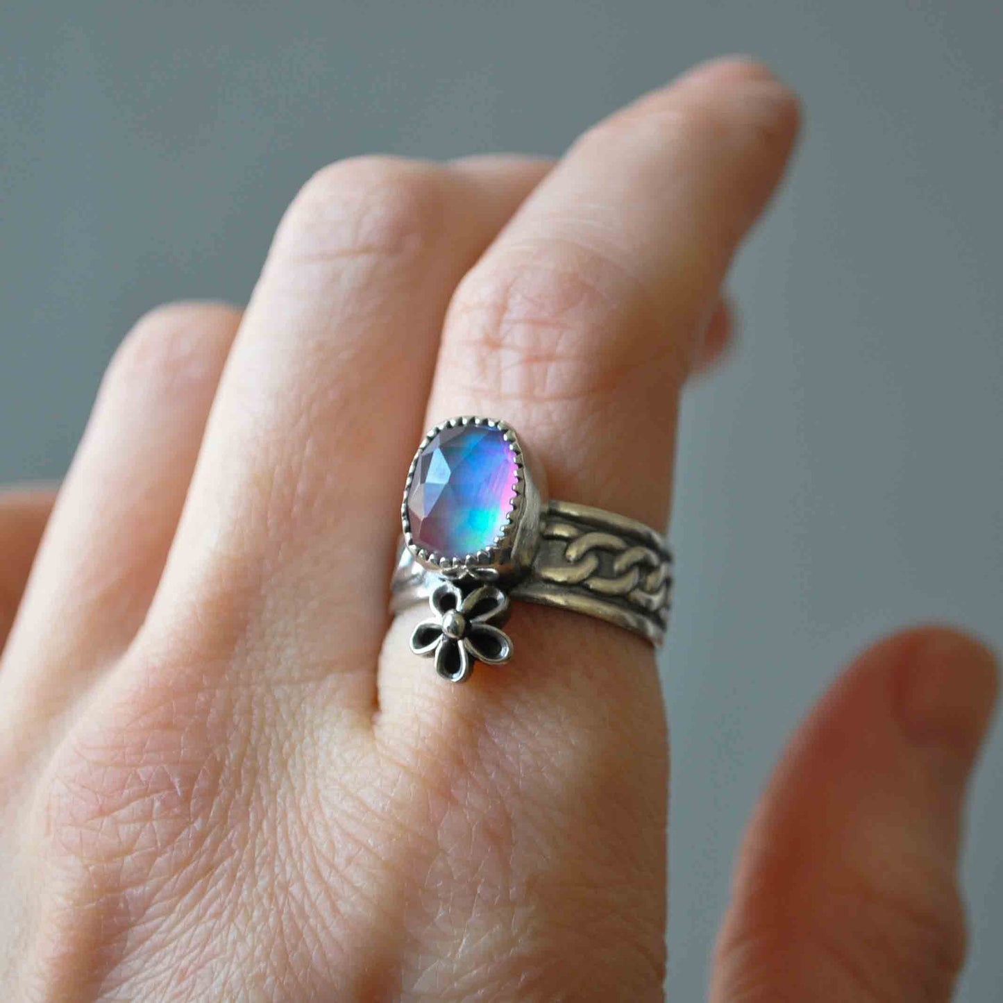 Hand wearing two rings with a colorful gemstone on a neutral background