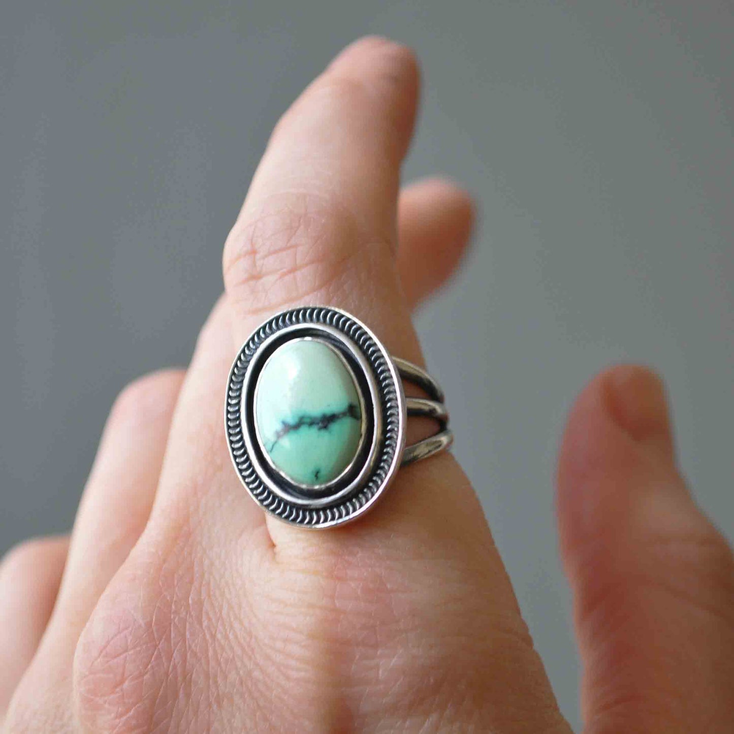 Silver ring with a turquoise stone on a finger against a neutral background