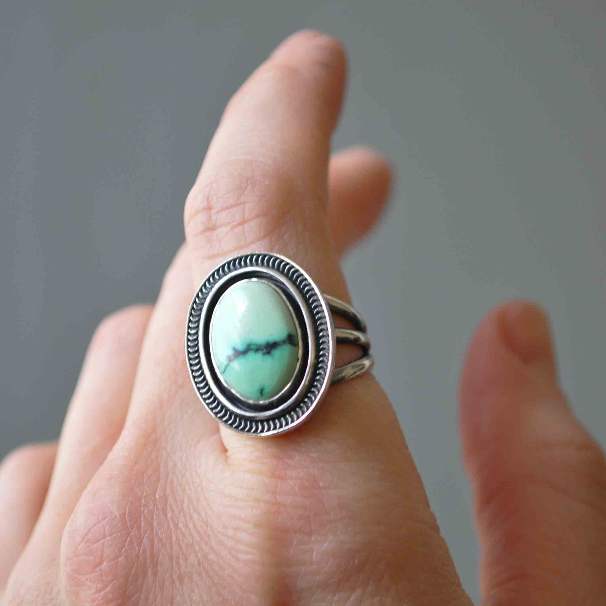 Silver ring with a turquoise stone on a finger against a neutral background
