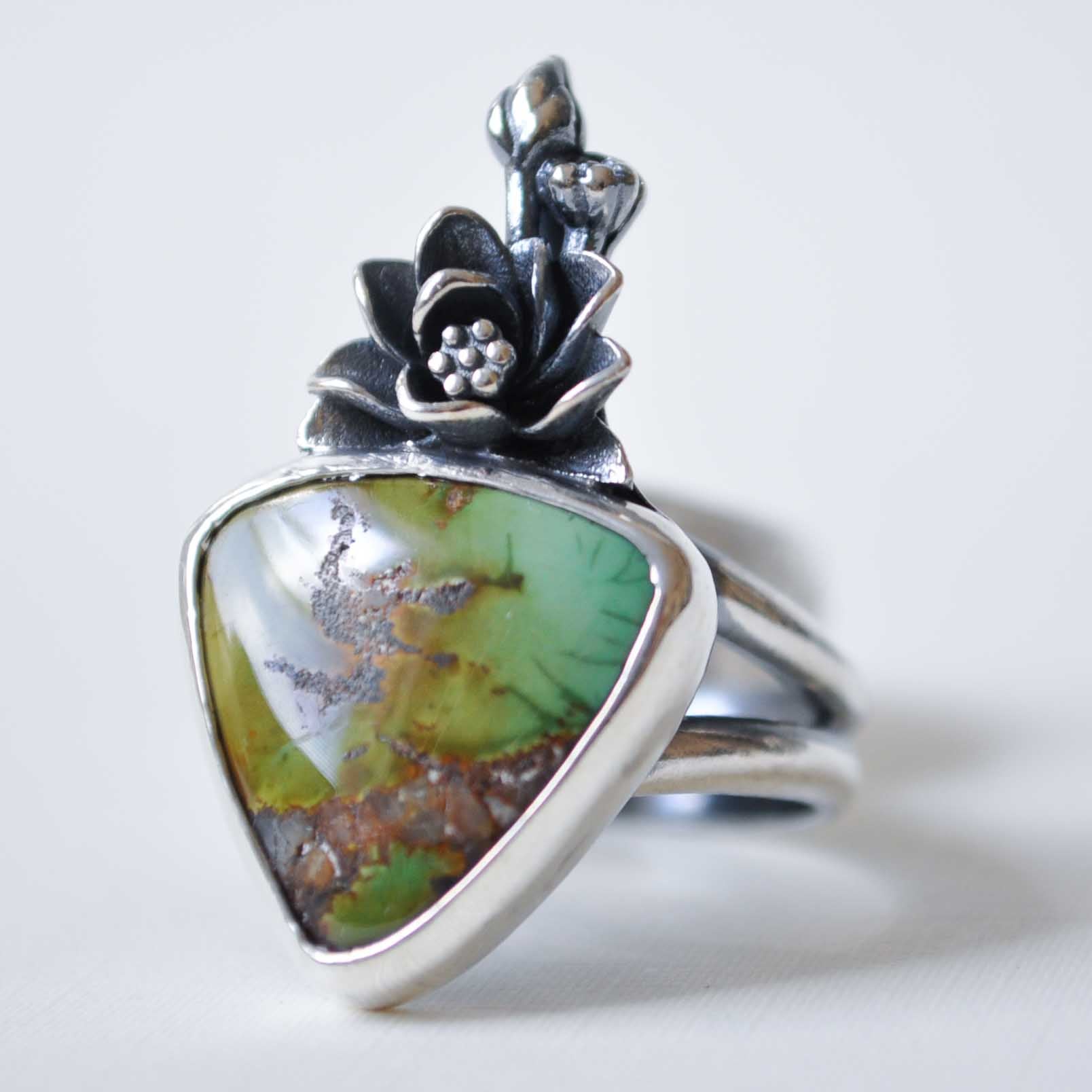Silver ring with a green stone and floral design on a white background