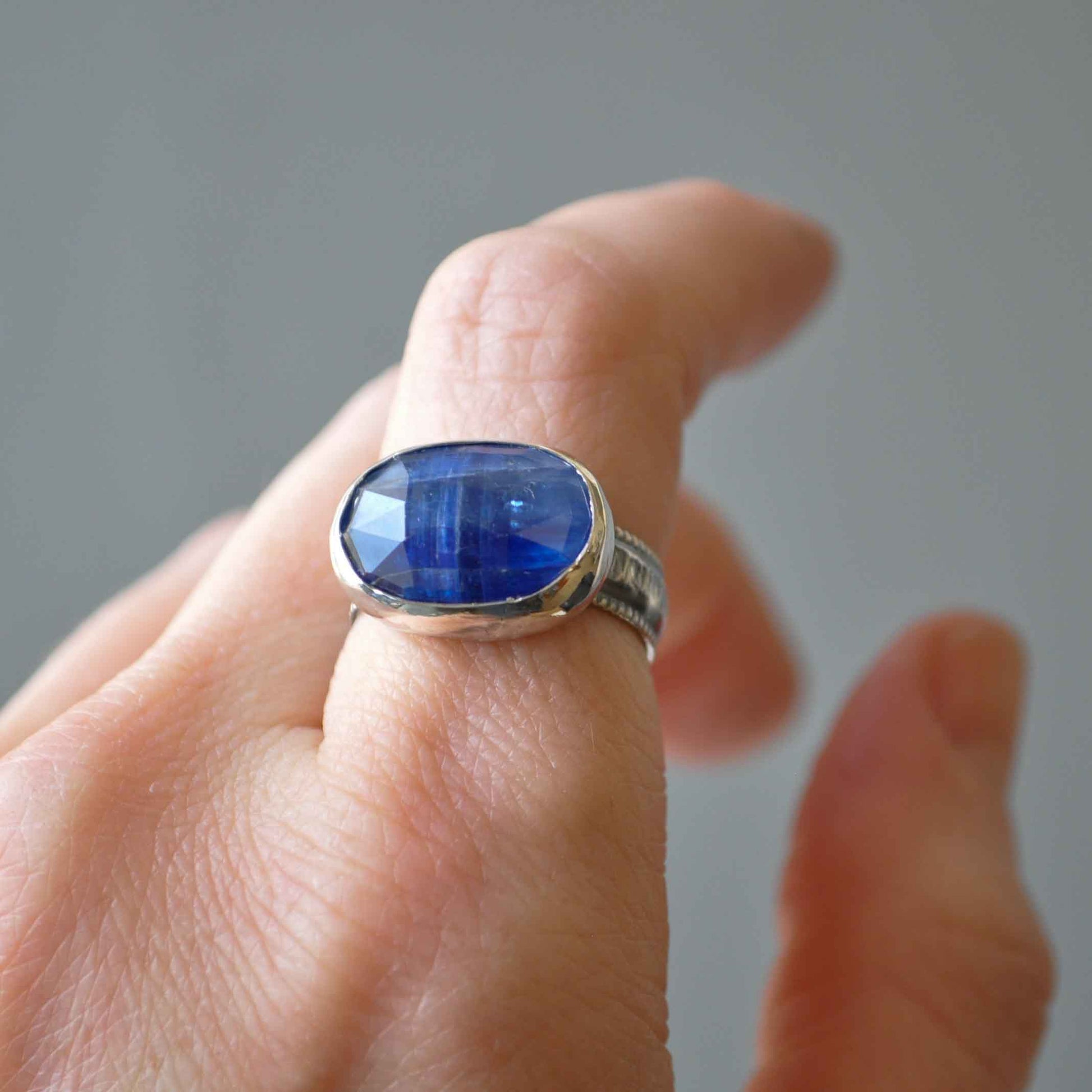 Silver ring with a blue gemstone on a finger against a neutral background