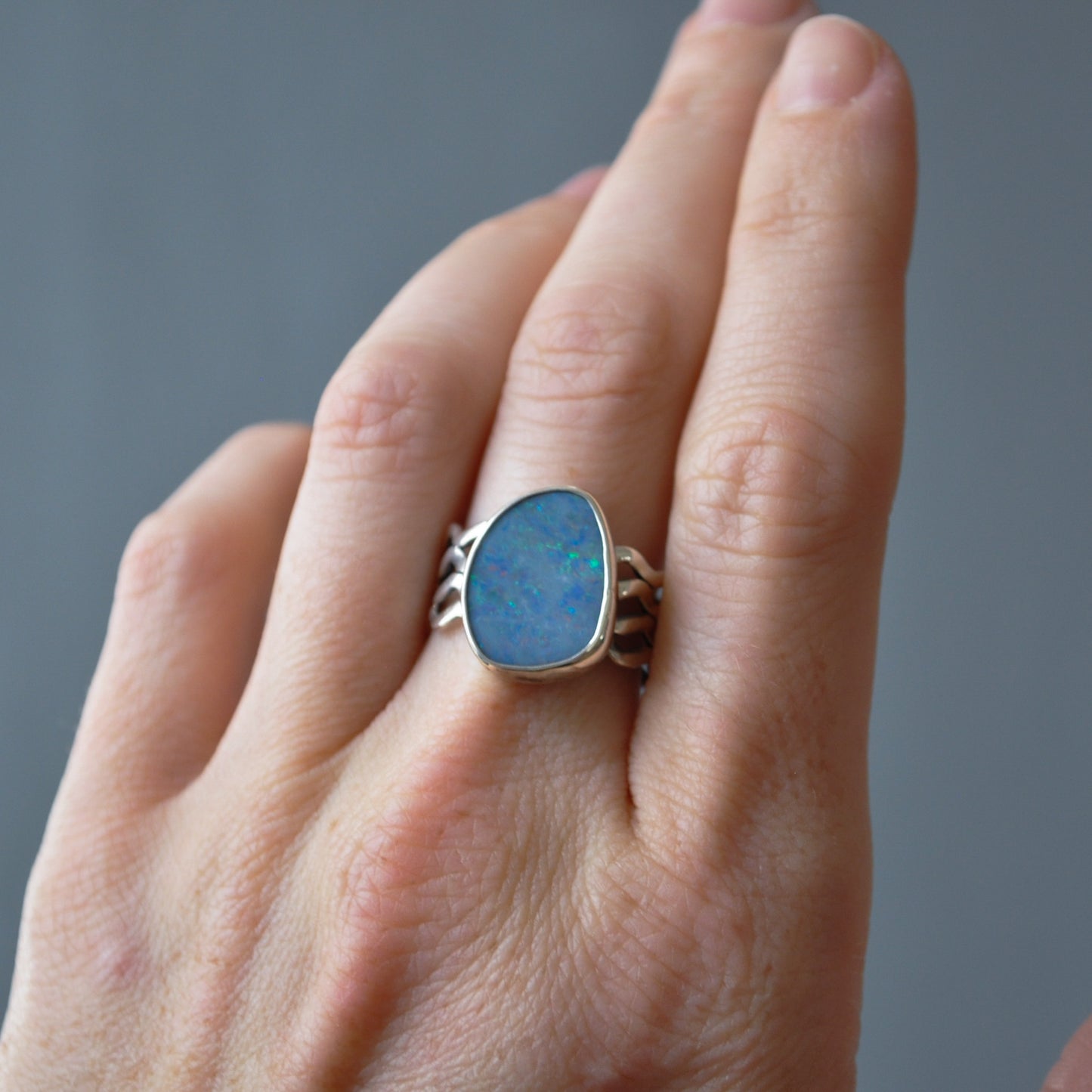 A close-up of a hand wearing a silver ring with a large, irregular-shaped blue opal gemstone.