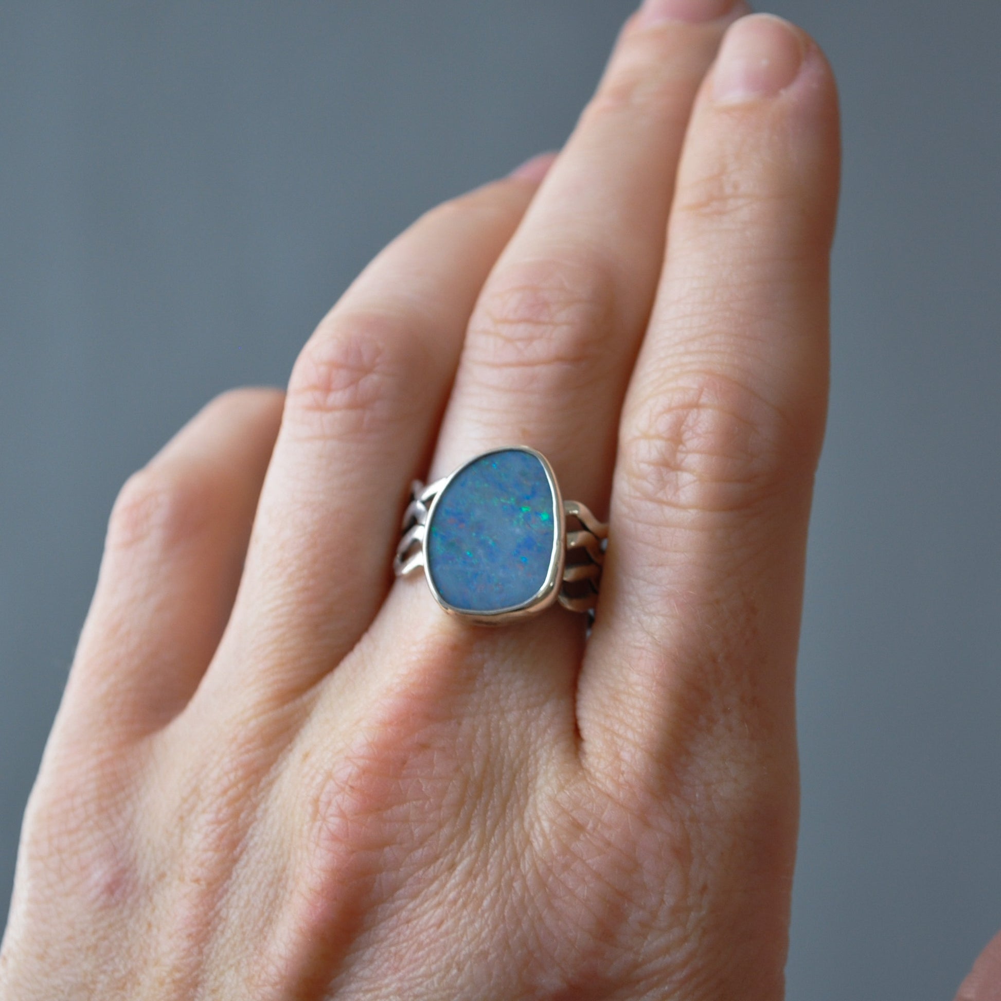 A close-up of a hand wearing a silver ring with a large, irregular-shaped blue opal gemstone.