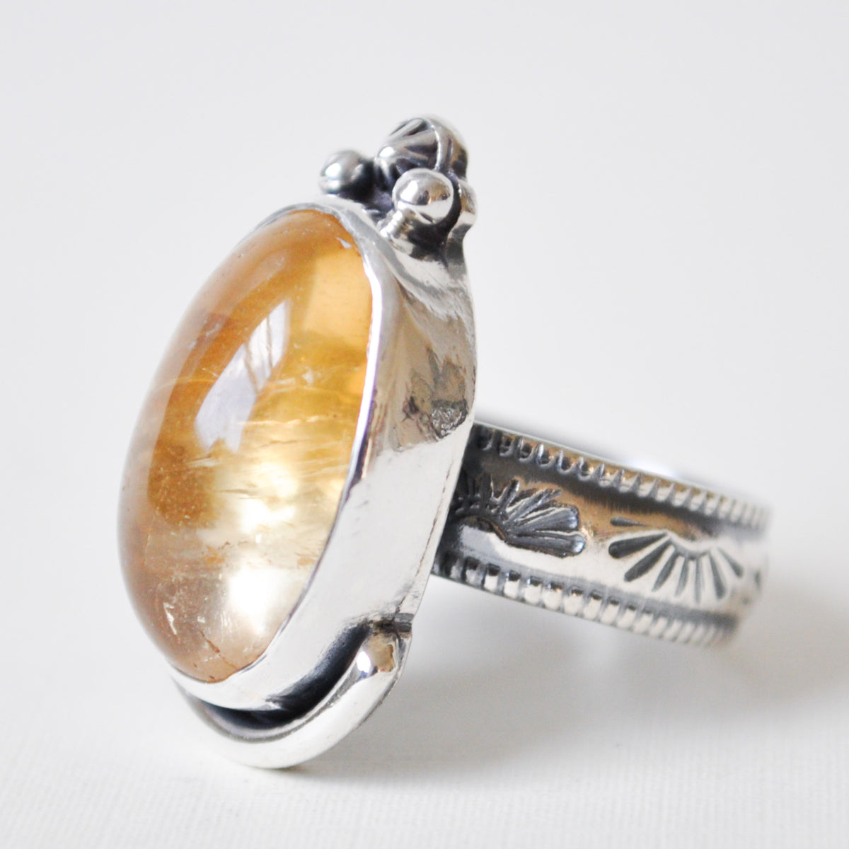 A sterling silver ring featuring a large, polished oval citrine cabochon gemstone with a warm golden-brown hue and natural inclusions, set against a clean white background.