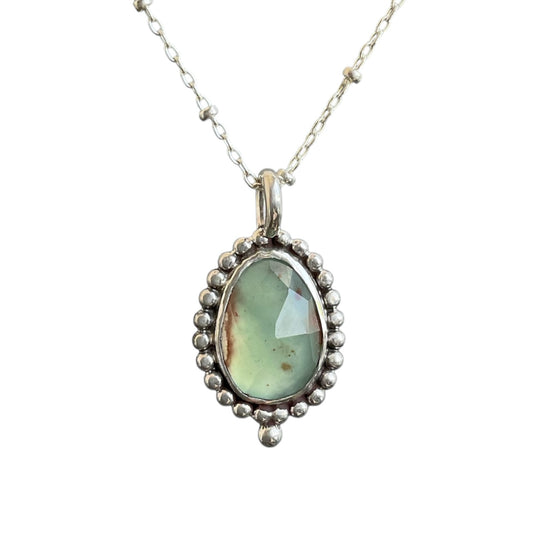 Silver pendant with a green gemstone on a white background