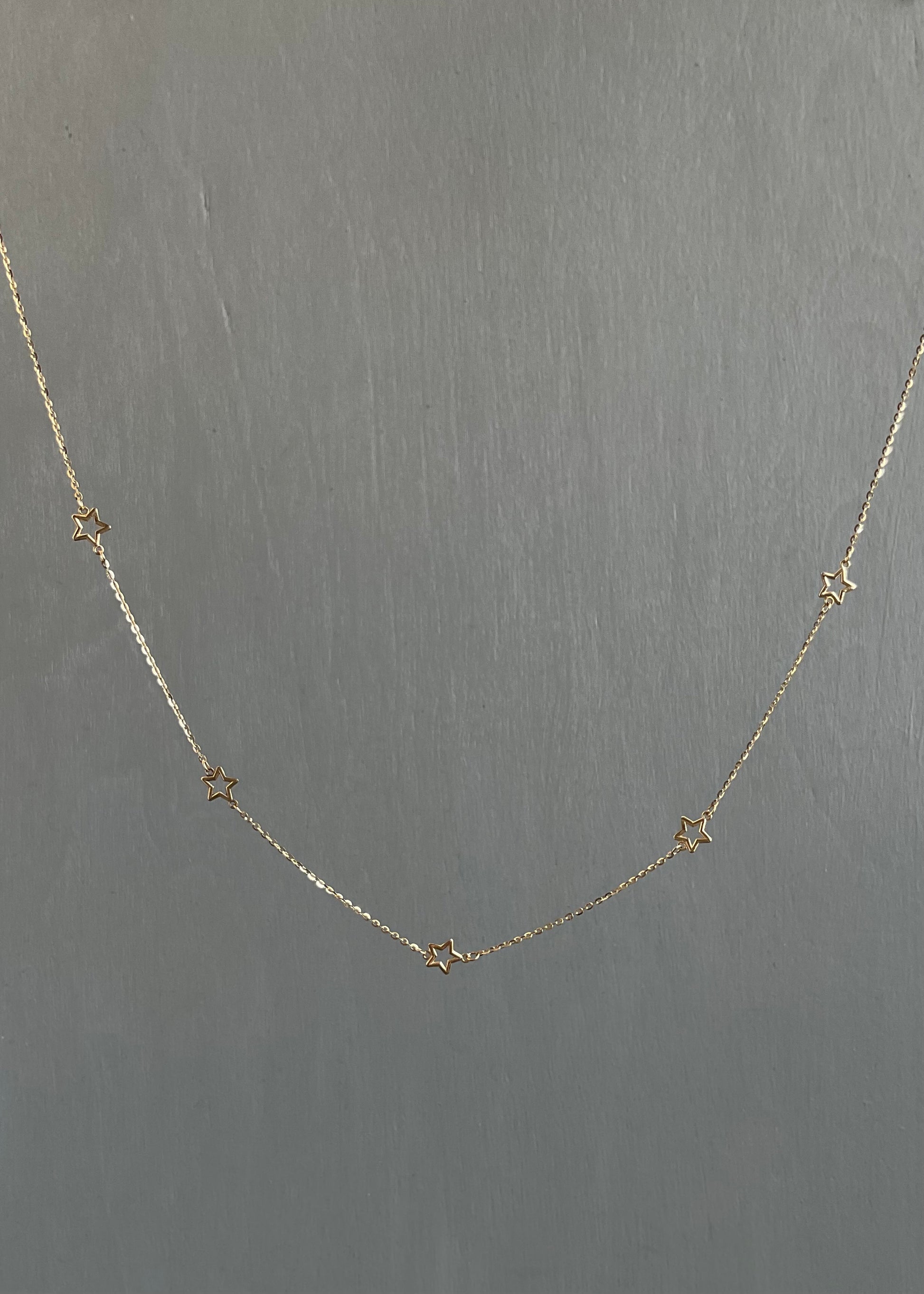 Delicate gold necklace with star-shaped pendants on a gray background