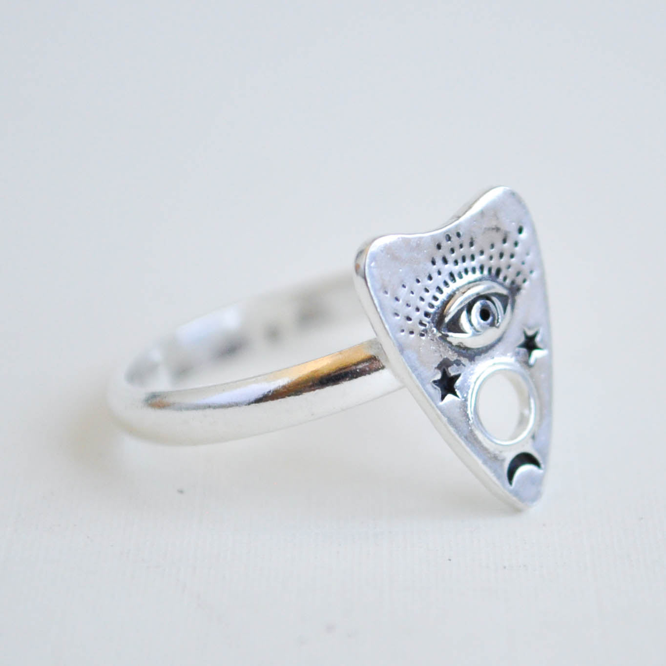 Silver triangle-shaped ring with eye design on a light gray background
