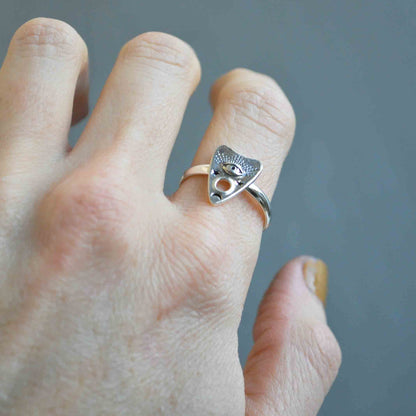 Silver ring with a unique design worn on a finger against a blurred background