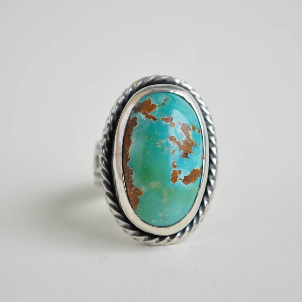 Chunky turquoise gemstone with a twisted frame and a chain patterned ring band, in sterling silver.