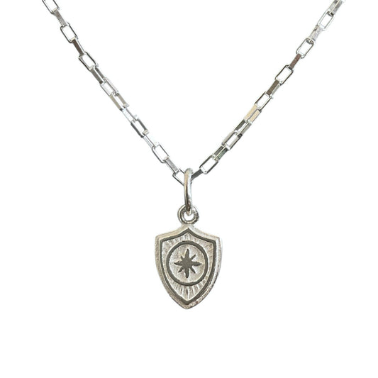 Sterling silver shield charm hanging on a baby paper clip chain.