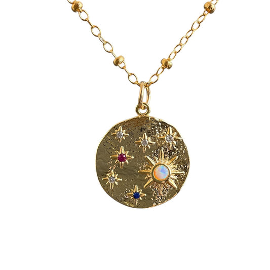 Gold necklace with a circular pendant featuring milkyway star designs and gemstones on a white background
