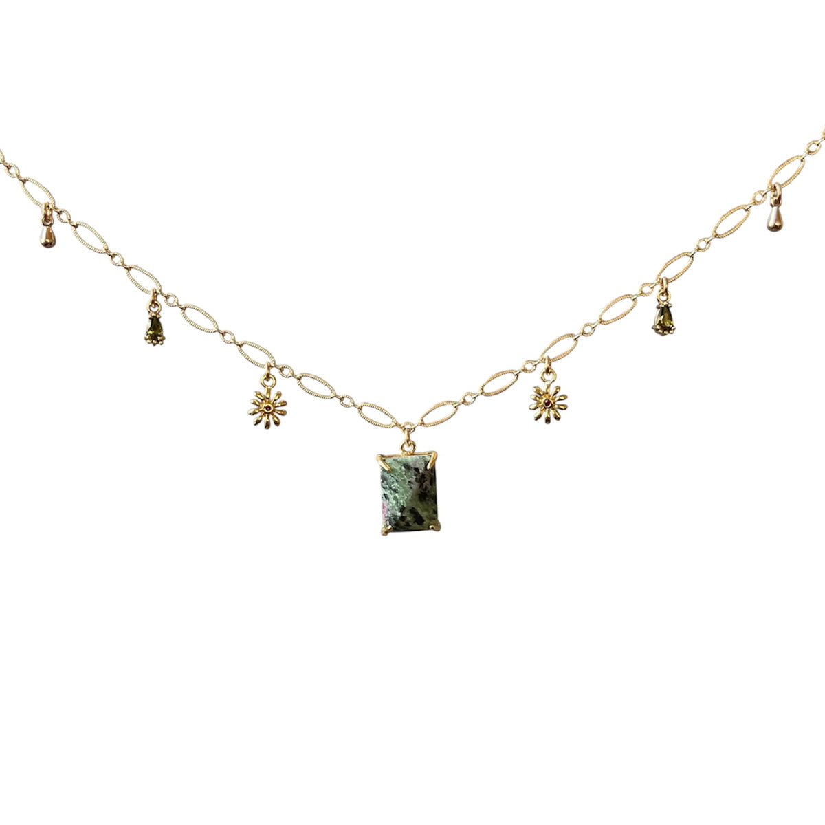 A gold chain necklace featuring a central rectangular green gemstone pendant and small dangling floral and tassel charms, displayed against a solid white background.