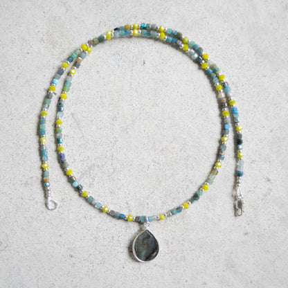 Beaded blue and green necklace with a teardrop pendant on a light gray background