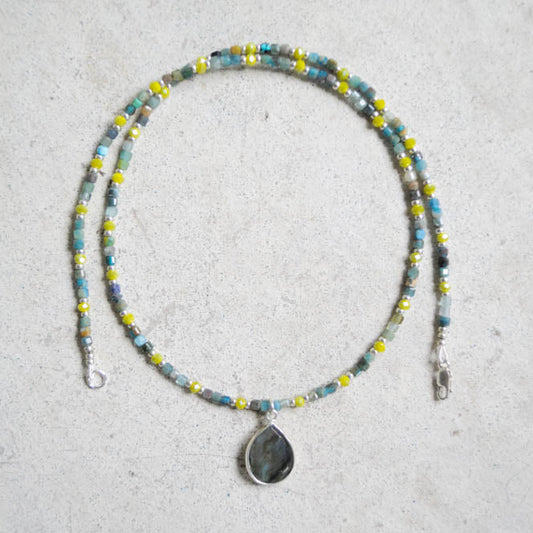 Beaded blue and green necklace with a teardrop pendant on a light gray background