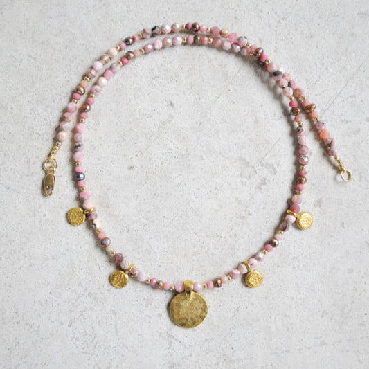 Rhodochrosite beaded necklace with gold coins on a textured surface