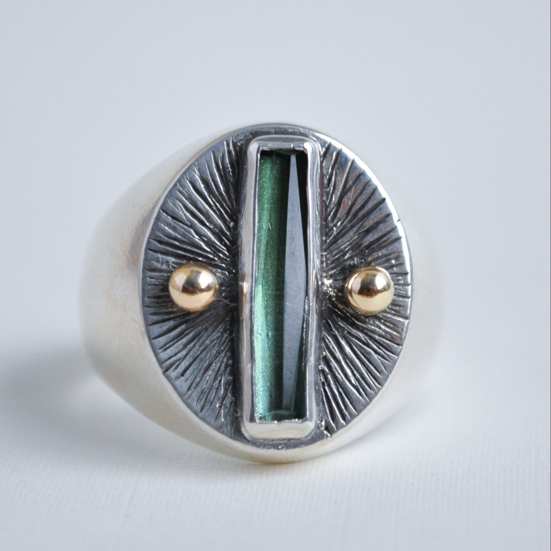 Silver ring with green central stone and gold accents on a light gray background