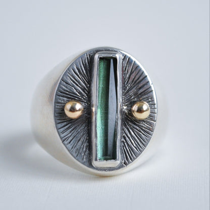 Silver ring with green central stone and gold accents on a light gray background
