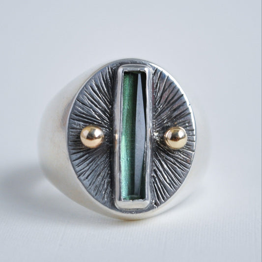 Silver ring with green central stone and gold accents on a light gray background