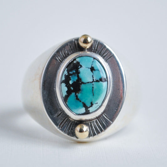 Silver ring with turquoise stone and gold accents on a light gray background