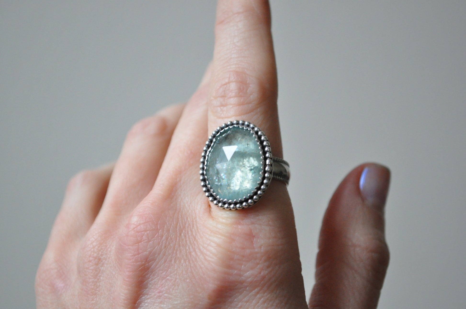Hand wearing a ring with a green gemstone on a neutral background