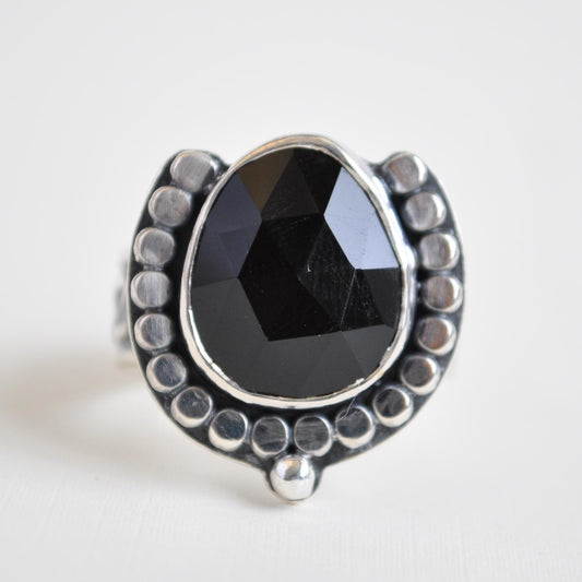 Silver ring with a black gemstone on a light gray background