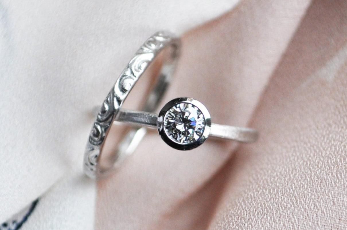 Silver ring with a diamond against a neutral cloth background