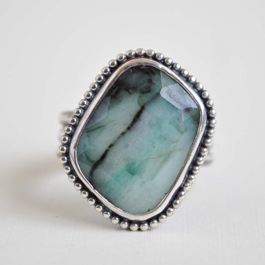 Ring with a large green stone and silver beaded band on a light background