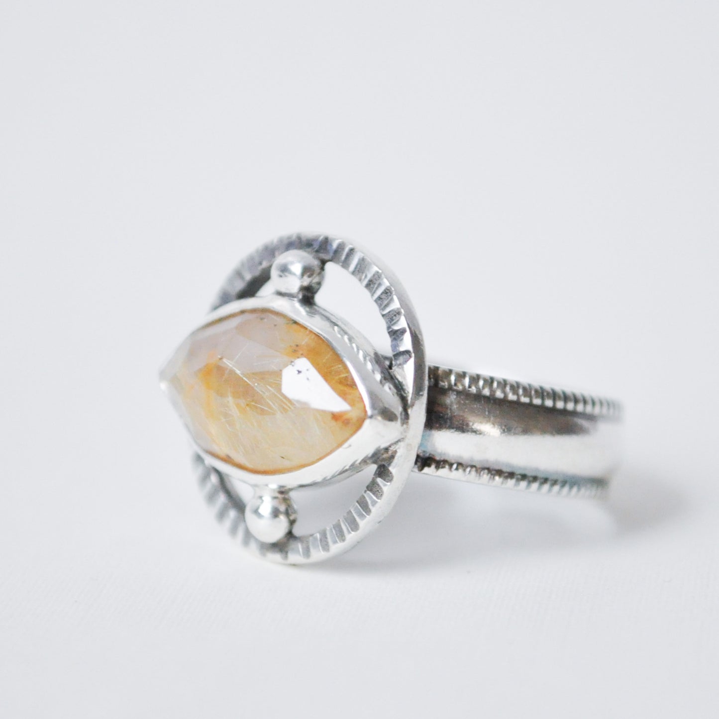Silver ring with a large, faceted stone on a light gray background