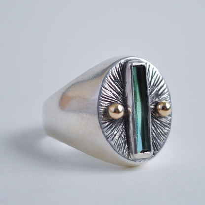 Silver ring with a green stone and gold accents on a light gray background