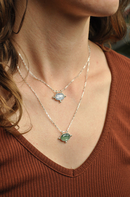 Close-up of a person wearing two necklaces with gemstones on a brown shirt.