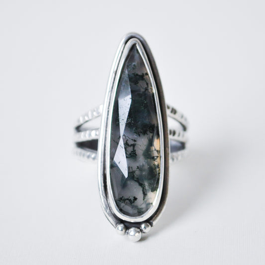 Silver ring with a large, teardrop-shaped black stone on a light gray background