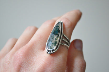 Silver ring with a stone on a finger against a neutral background