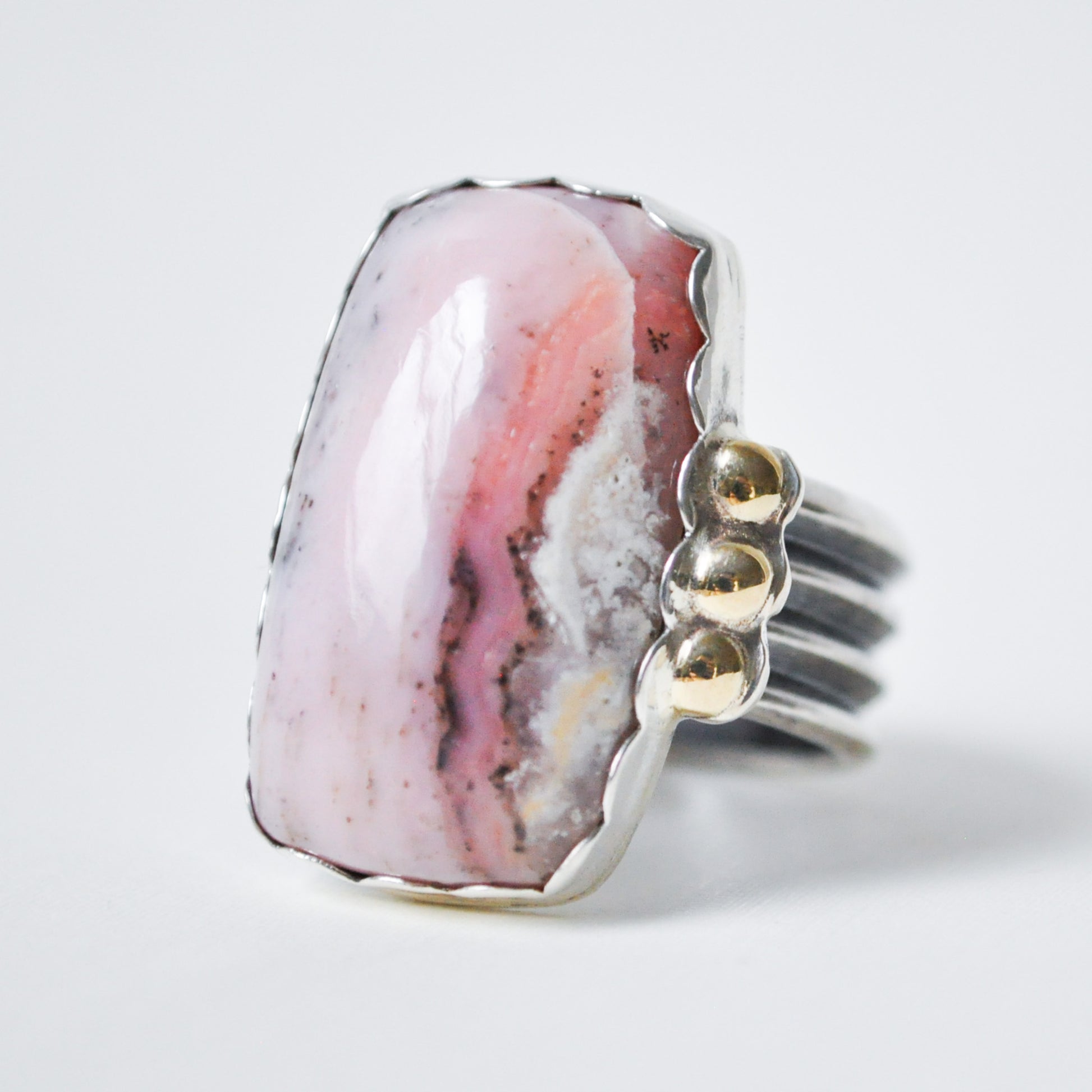 Ring with a pink and white stone and gold accents on a light gray background